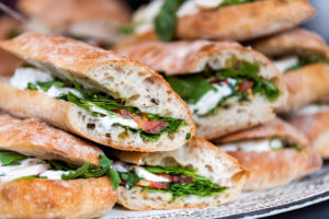 Closeup of fresh display of stacked pile of panini bread, mozzarella melted cheese, vegetarian italian tomatoes, basil lettuce in store, shop, cafe buffet catering sandwiches - Paulines Catering Natick MA